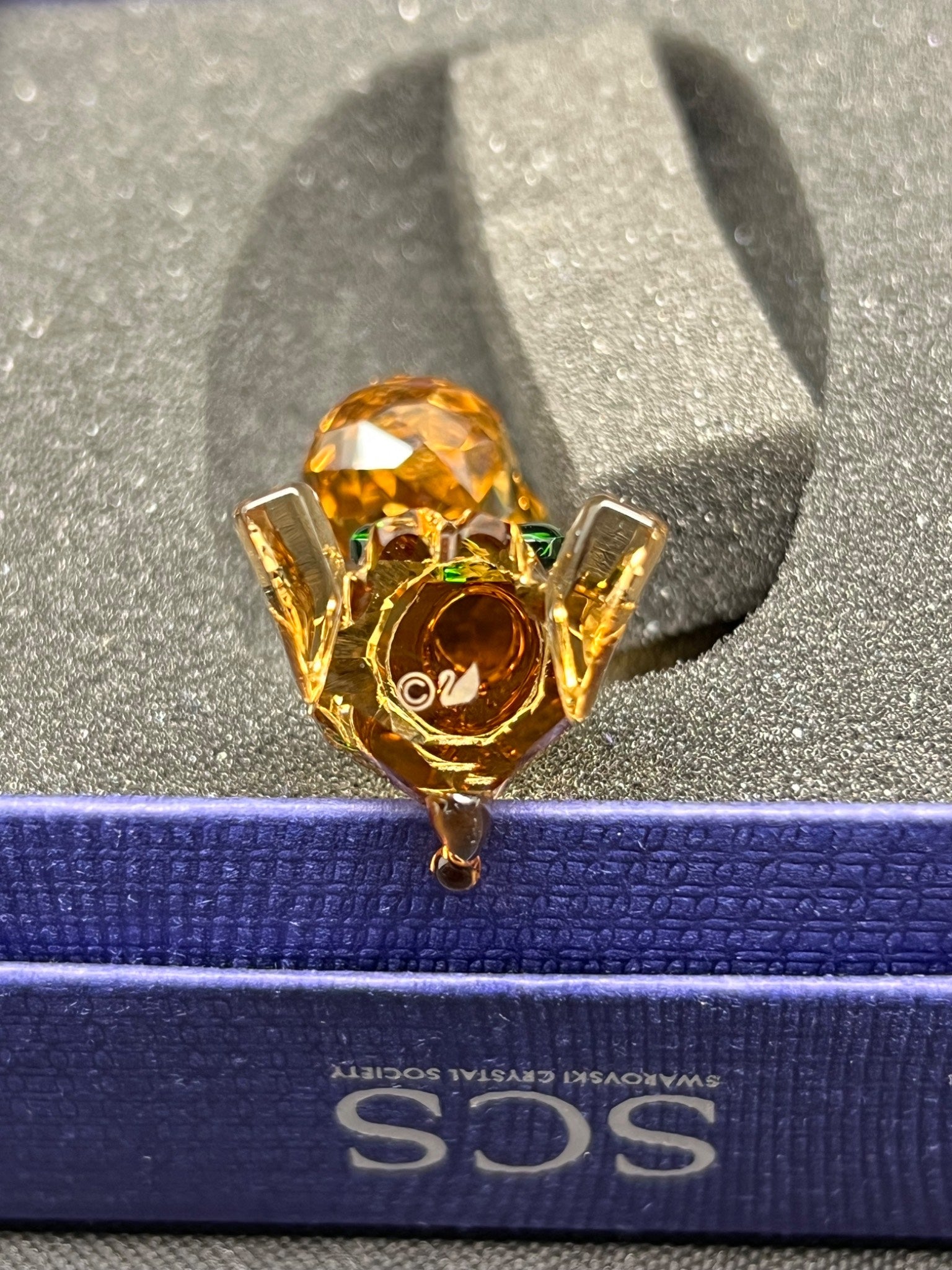 Gold brooch with a large amber-colored gemstone on a blue and silver background