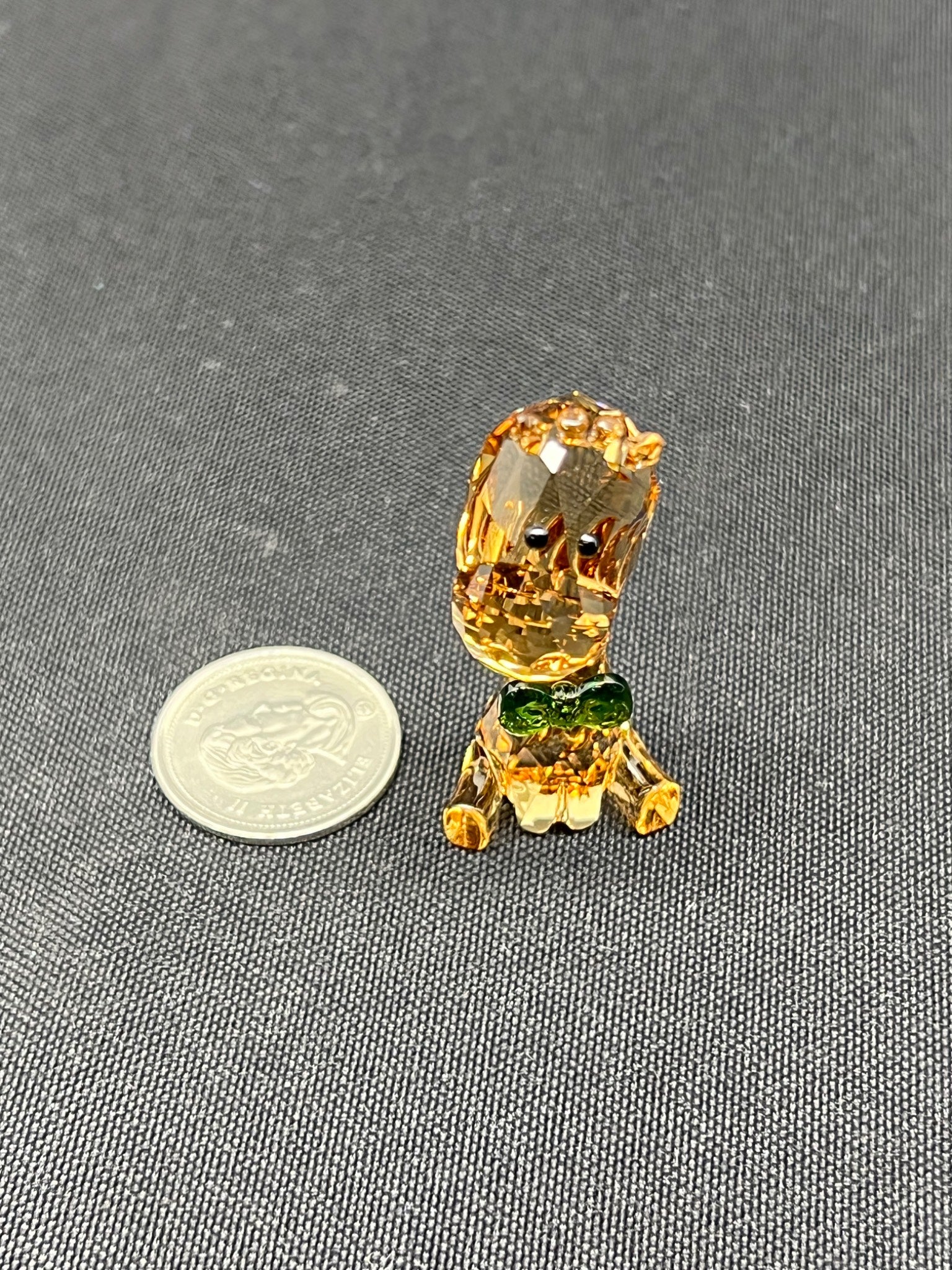 Small glass figurine of a lion with a coin for scale on a gray background