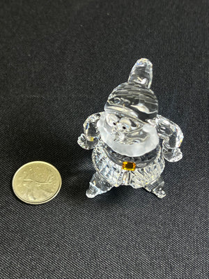 Crystal gnome figurine next to a coin on a black background