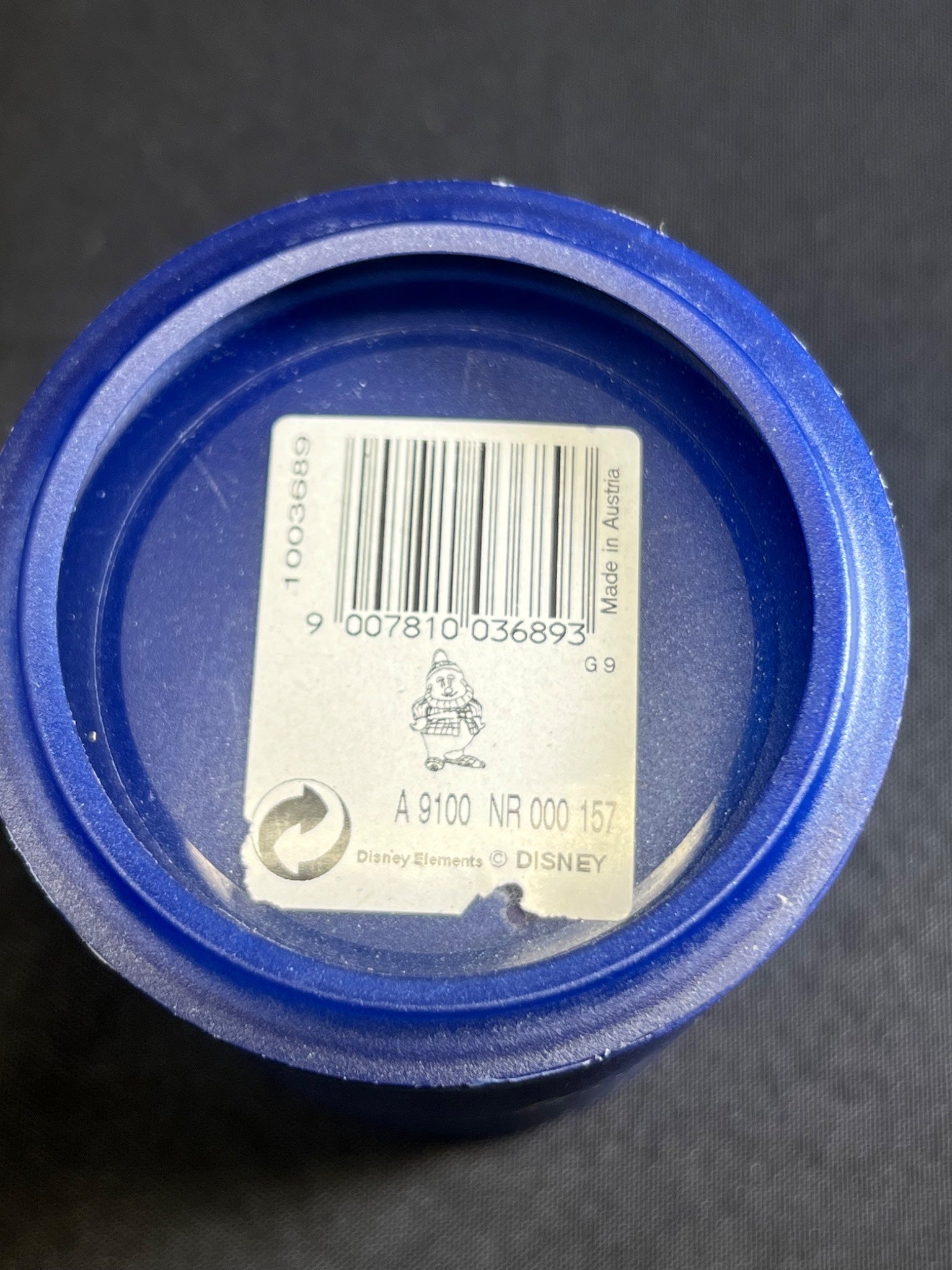 Close-up of a blue container lid with a barcode label on a dark background