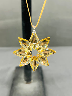 Star-shaped yellow gemstone pendant on a chain against a neutral background