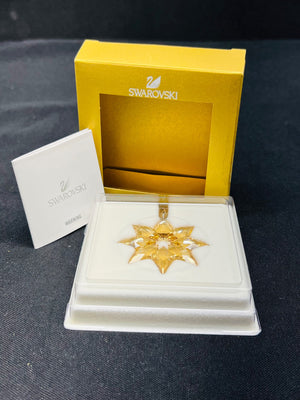 Gold star-shaped pendant with Swarovski packaging on a dark background