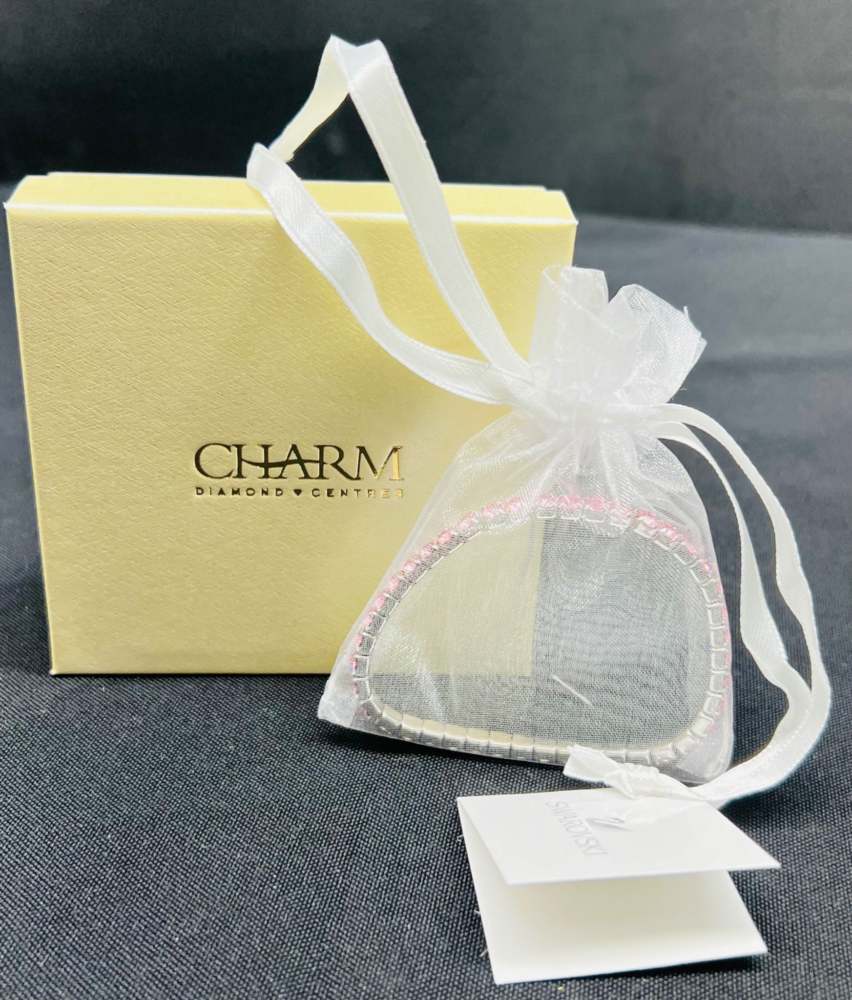 Heart-shaped jewelry box with a white ribbon and 'Charm' branding on a dark surface.