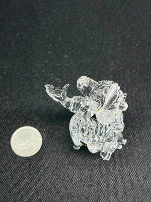 Clear glass figurine of a person on a horse next to a coin for scale on a dark background