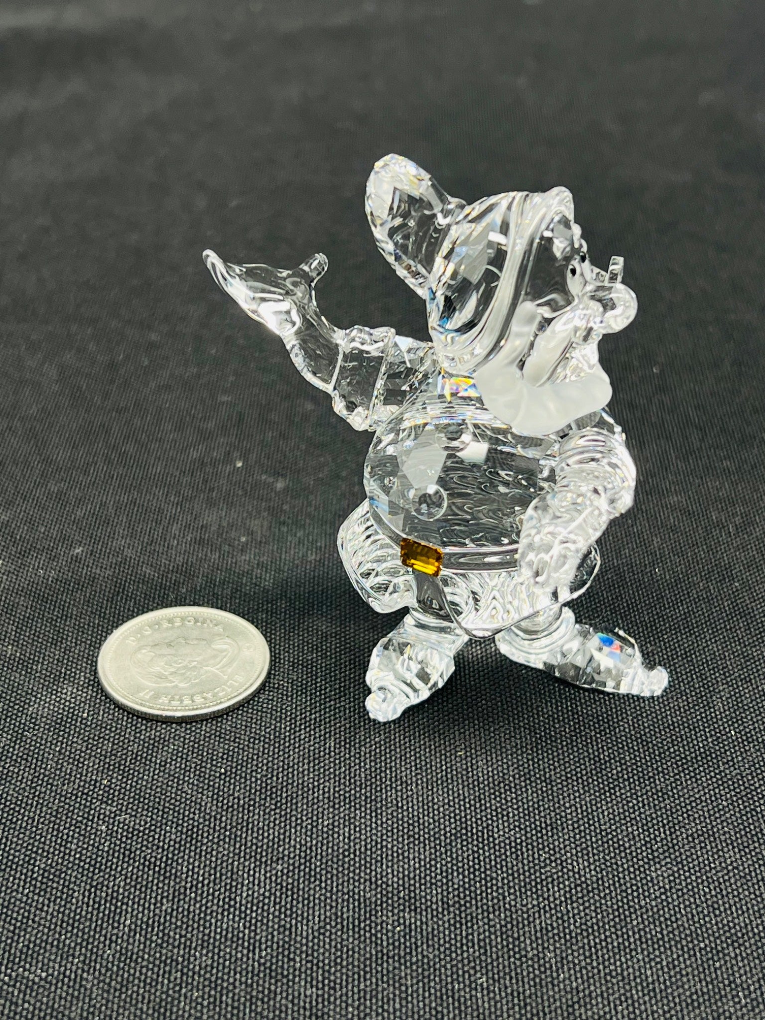 Clear crystal figurine of a character on a dark surface with a coin for scale.