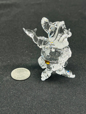 Clear crystal figurine of a character on a dark surface with a coin for scale.