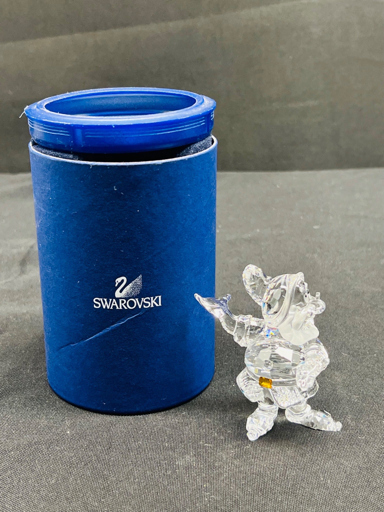 Swarovski branded blue cylindrical container with a clear crystal figurine on a gray surface