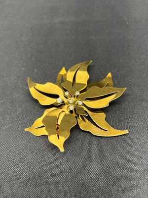 Gold flower-shaped brooch with embedded pearls on a gray background