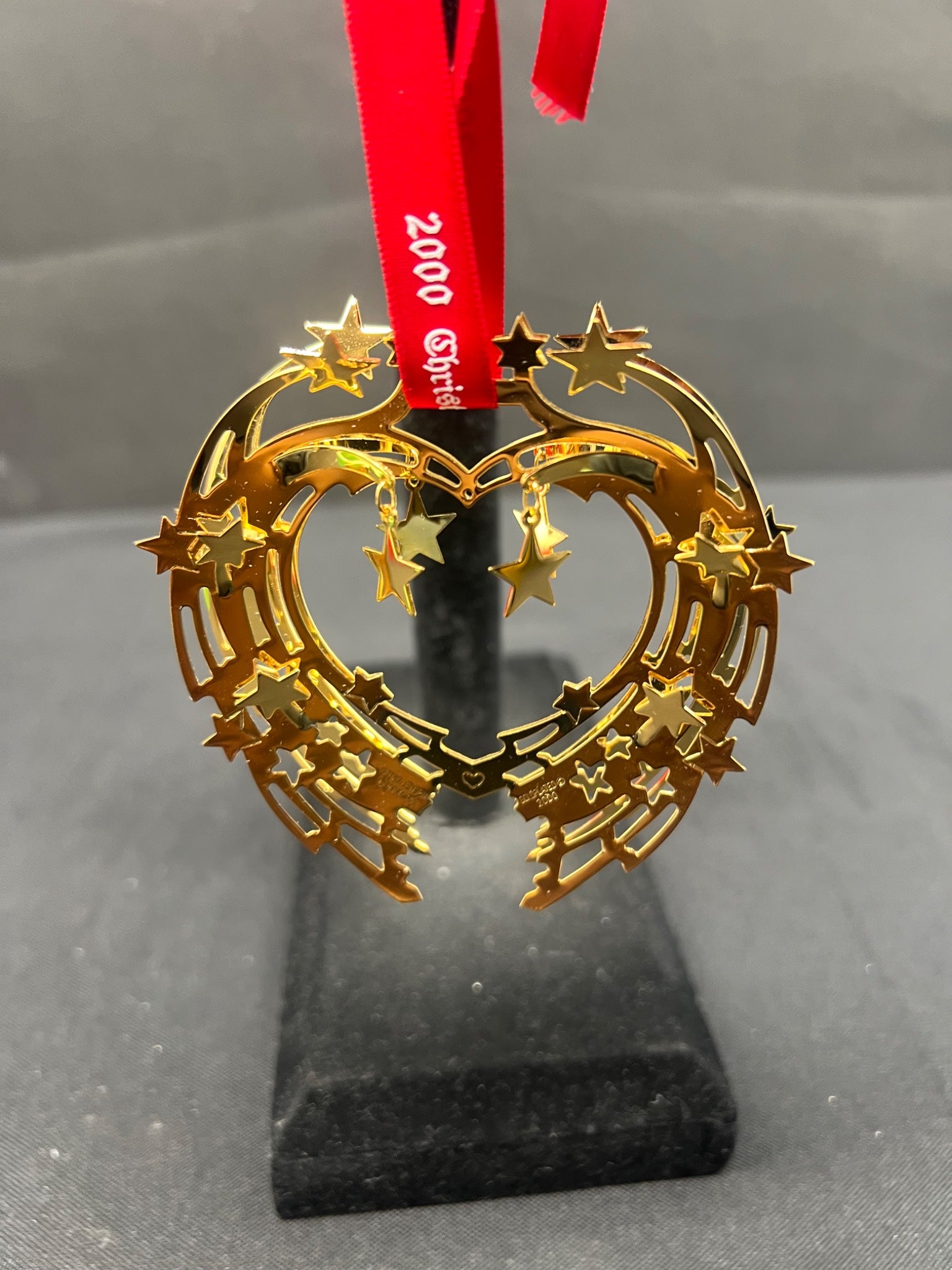 Gold star-shaped ornament on a stand with a red ribbon against a gray background