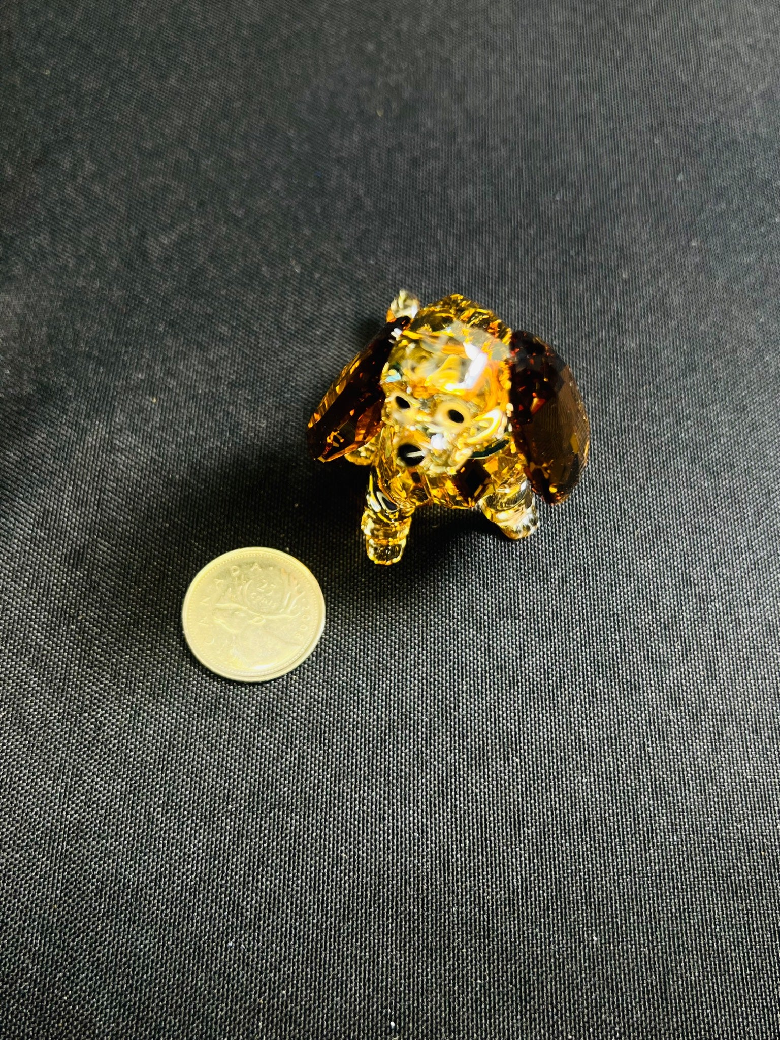 Gold elephant-shaped brooch on a dark fabric background with a coin for scale.