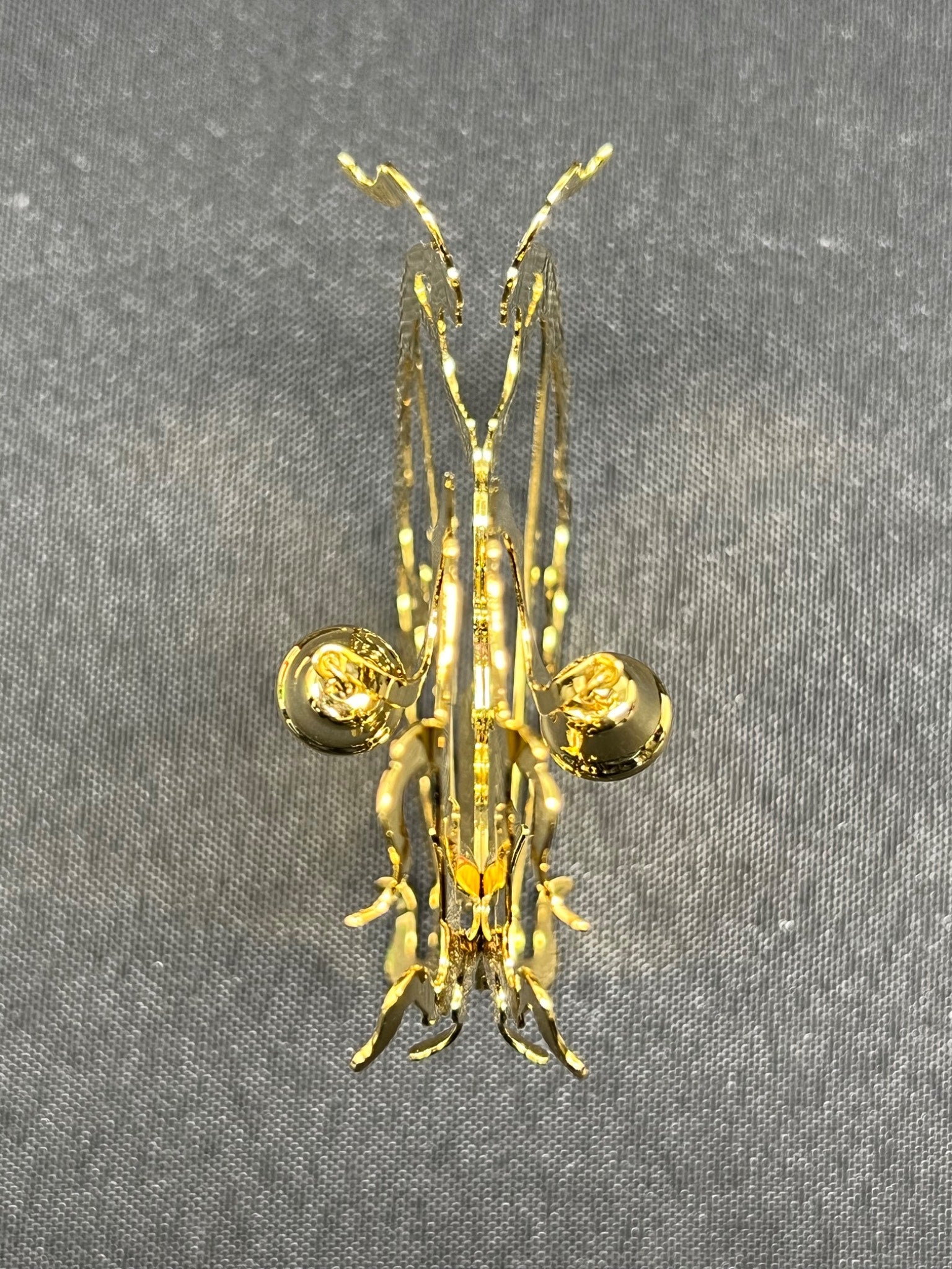 Gold-colored insect-shaped brooch on a gray fabric background