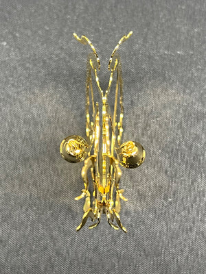 Gold-colored insect-shaped brooch on a gray fabric background