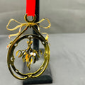 Gold Christmas ornament with mistletoe design on a red ribbon against a gray background