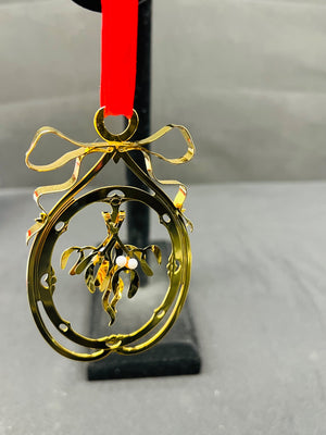 Gold Christmas ornament with mistletoe design on a red ribbon against a gray background
