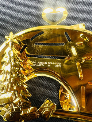 Gold pendant with 'Georg Jensen Denmark' engraving on a black background