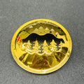 Gold-colored circular object with a mountain and tree design on a gray background