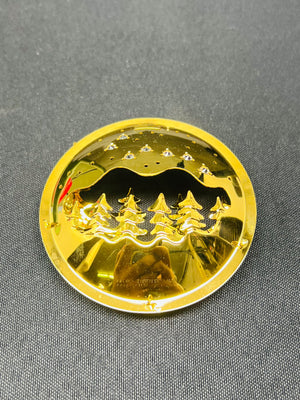 Gold-colored circular object with a mountain and tree design on a gray background