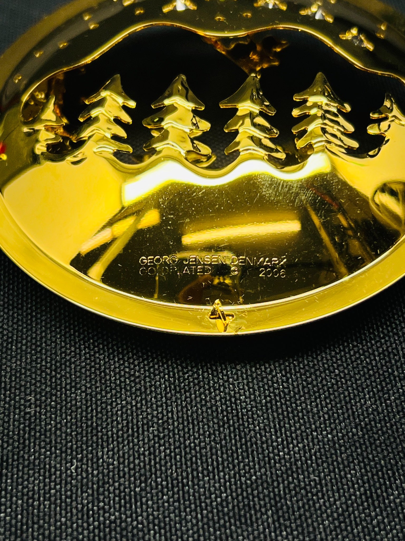 Gold-colored decorative item with a design on a dark fabric background