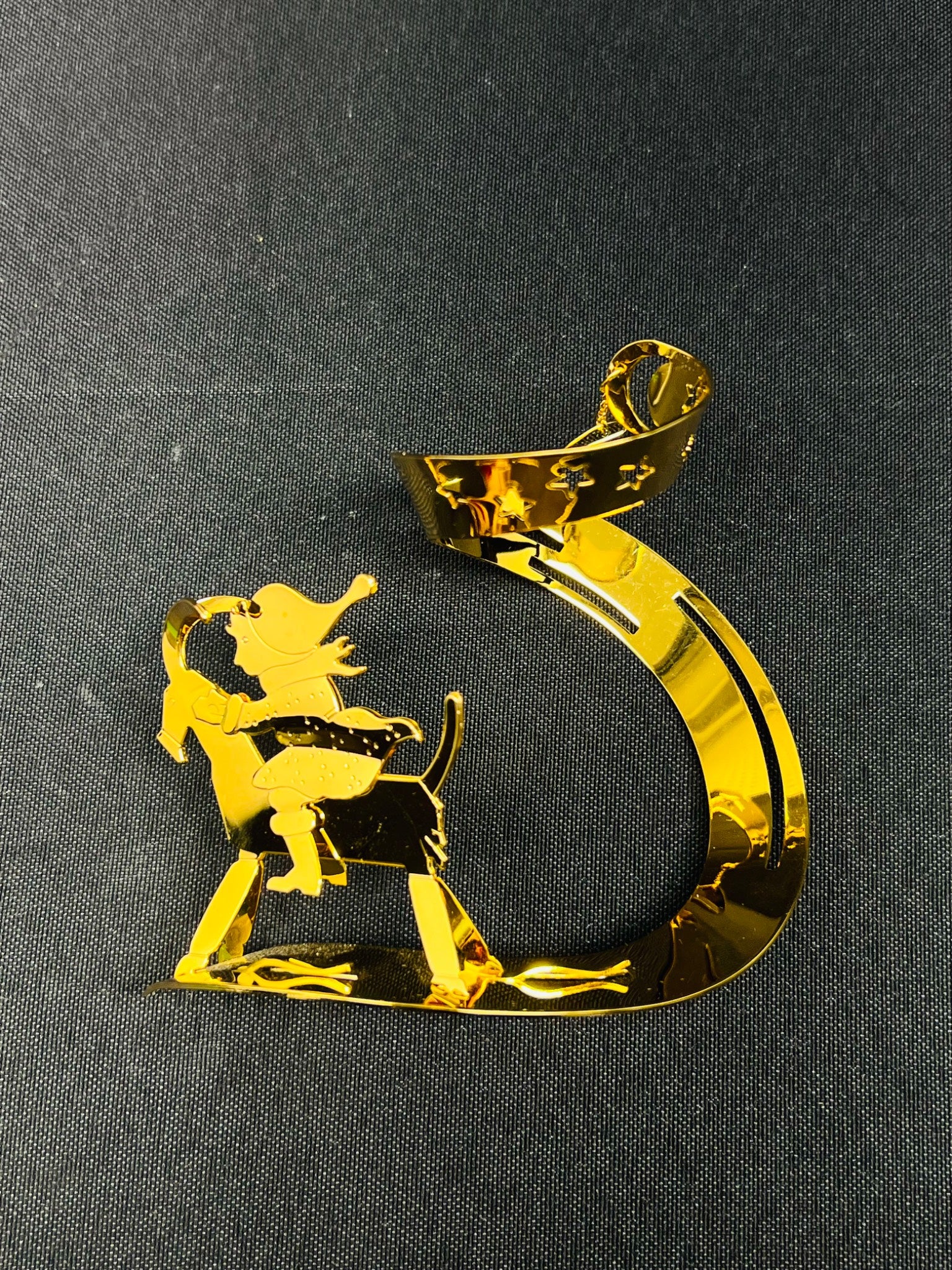 Gold decorative item shaped like a number '5' with a silhouette of a person on a horse against a black background
