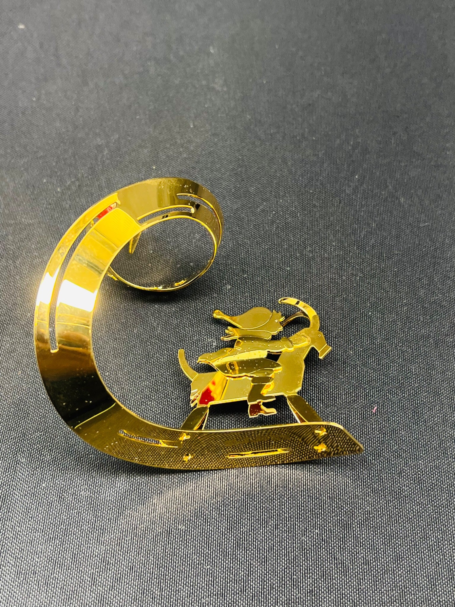 Gold metal dog figurine on a crescent moon against a gray background