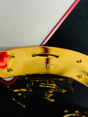 Gold belt buckle with 'Versace' branding on a dark surface