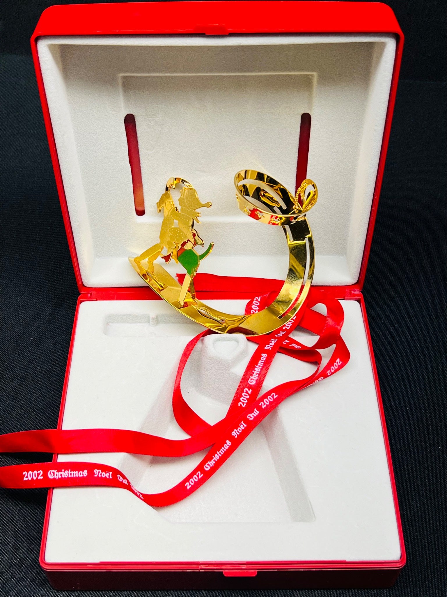 Gold ornament with red ribbon in an open red box on a black background