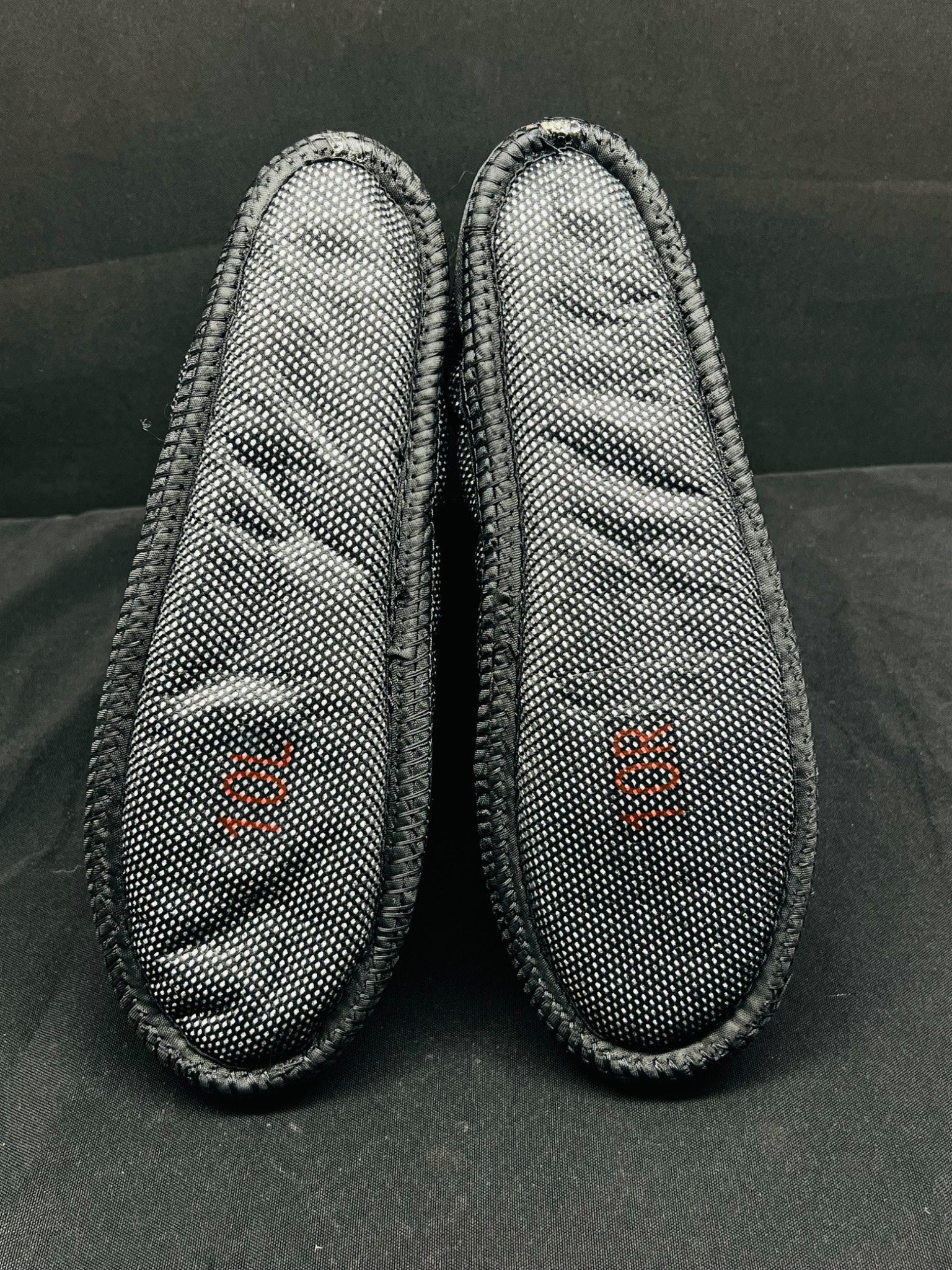 Two gray slippers with mesh design on a black background