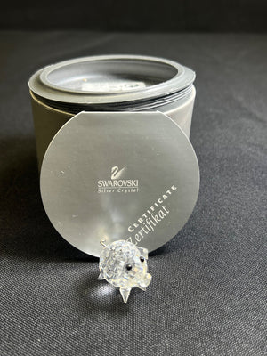 Swarovski crystal on a gray surface with a Swarovski branded container.