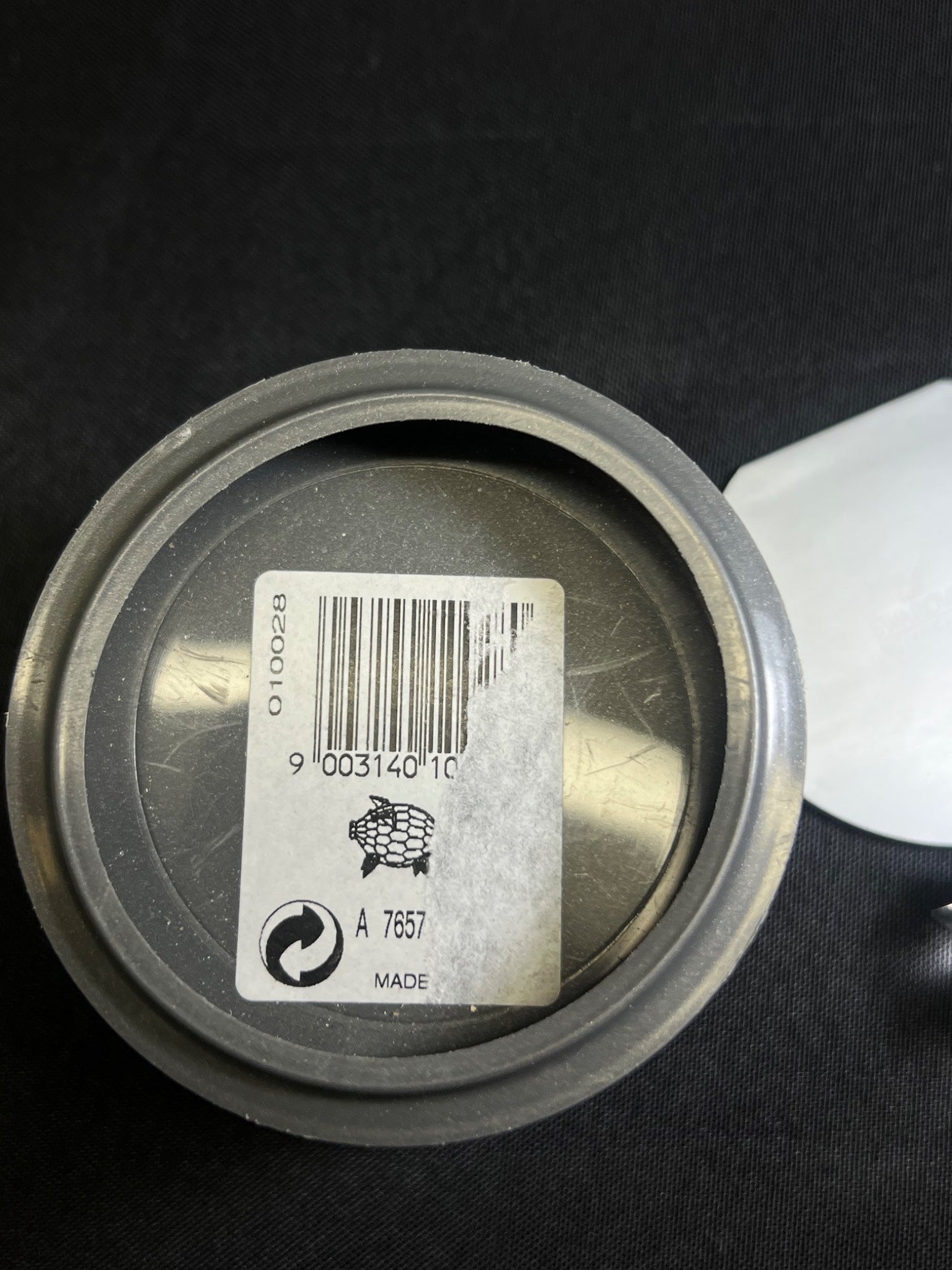 Close-up of a metal container lid with a barcode label on a black background