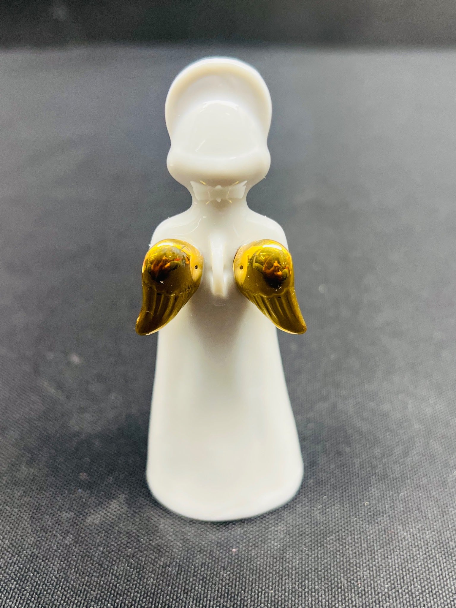 Small white figurine with gold wings on a gray background
