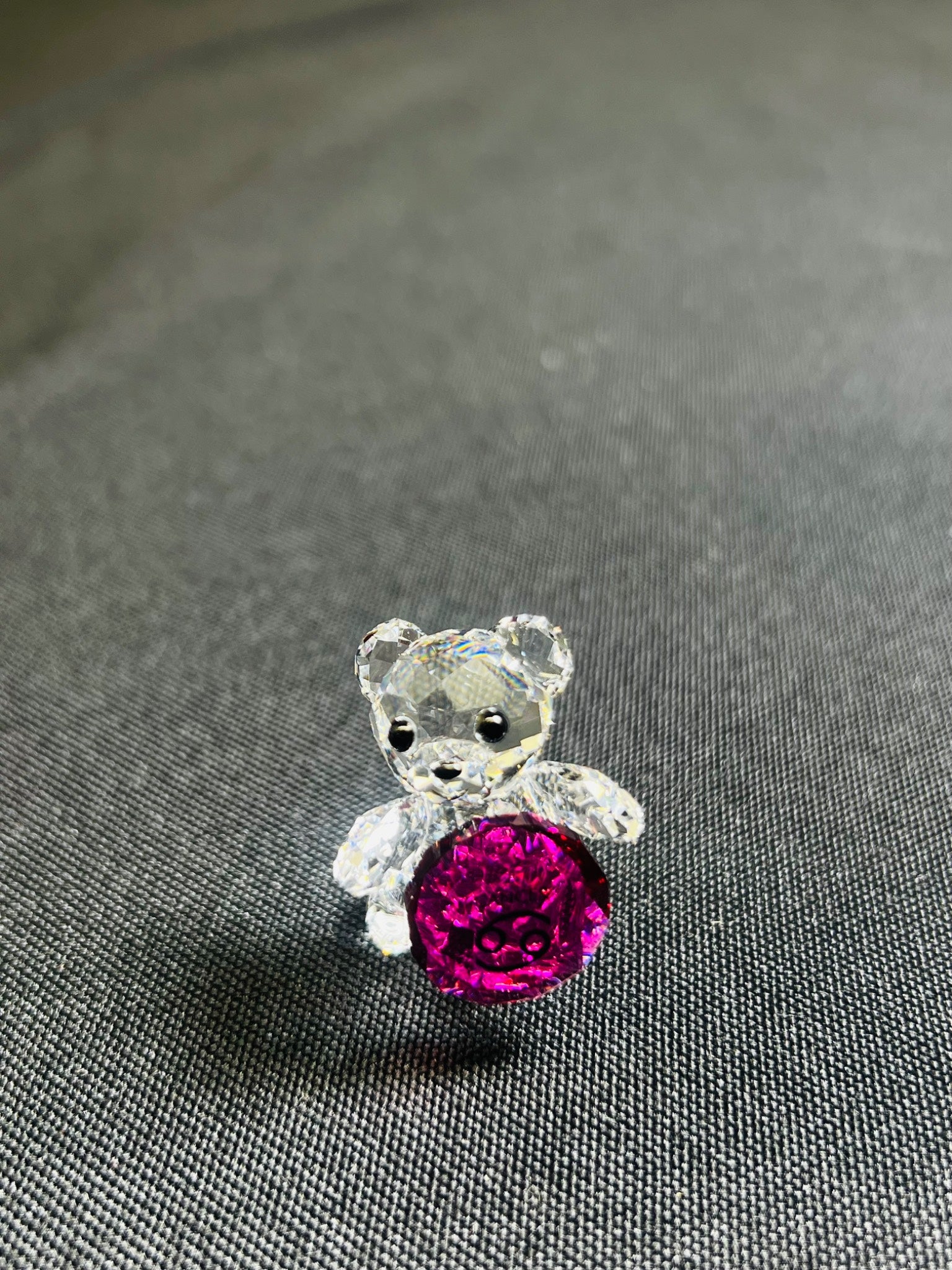 Crystal teddy bear with a pink gem on a gray fabric background