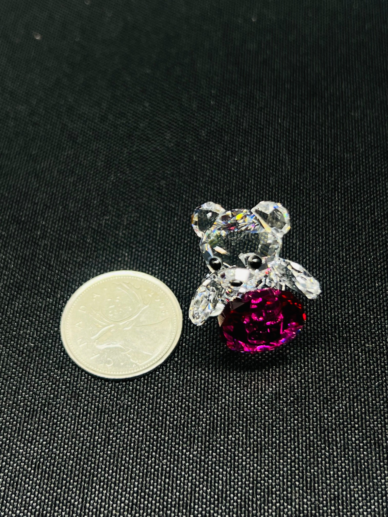 Crystal bear with a pink heart next to a coin on a black background