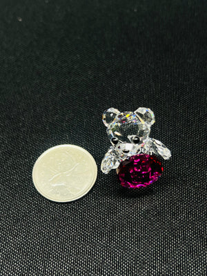 Crystal bear with a pink heart next to a coin on a black background