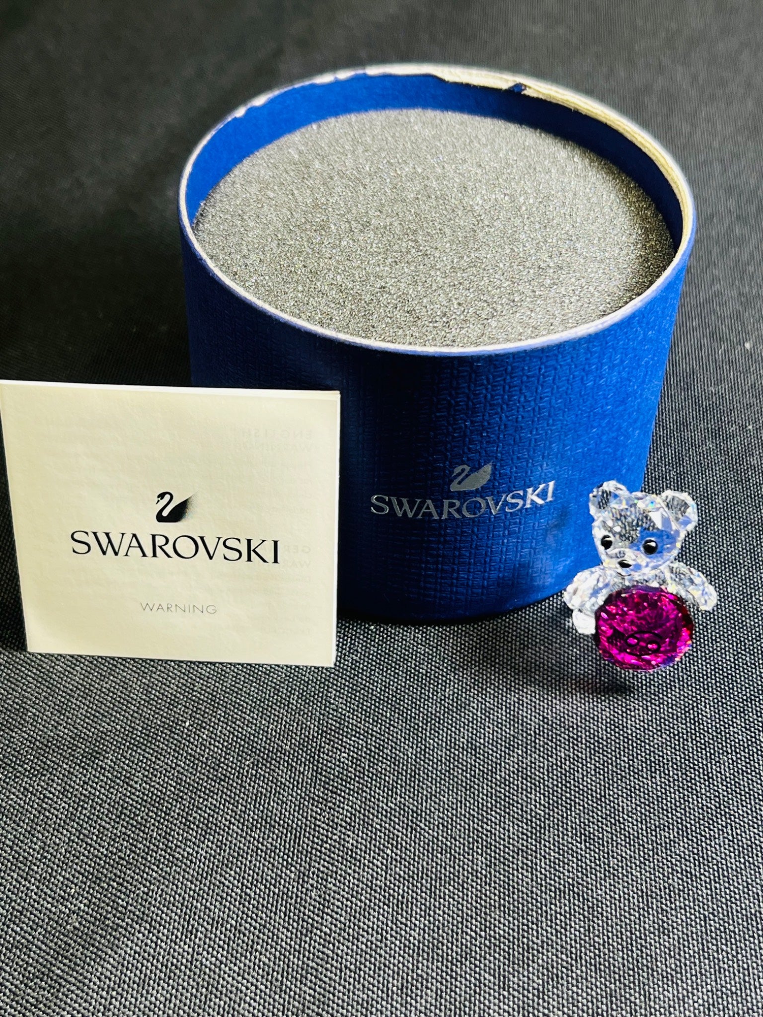 Swarovski teddy bear with pink gemstone in front of a blue Swarovski box on a gray surface.