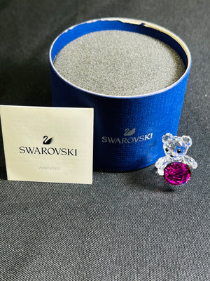 Swarovski teddy bear with pink gemstone in front of a blue Swarovski box on a gray surface.