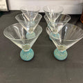 Set of five martini glasses with textured turquoise bases on a dark surface.