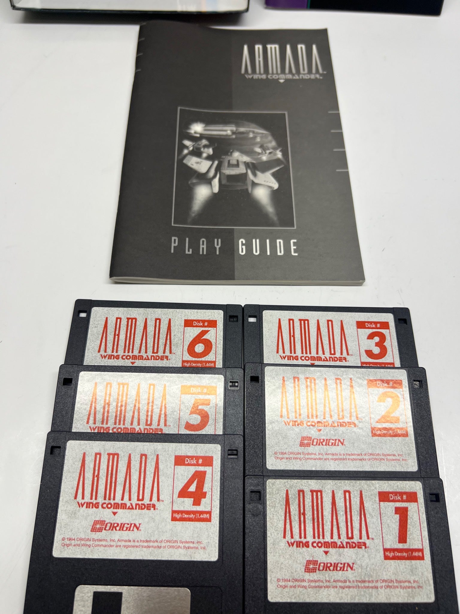 Collection of Armada video game disks and play guide on a white surface